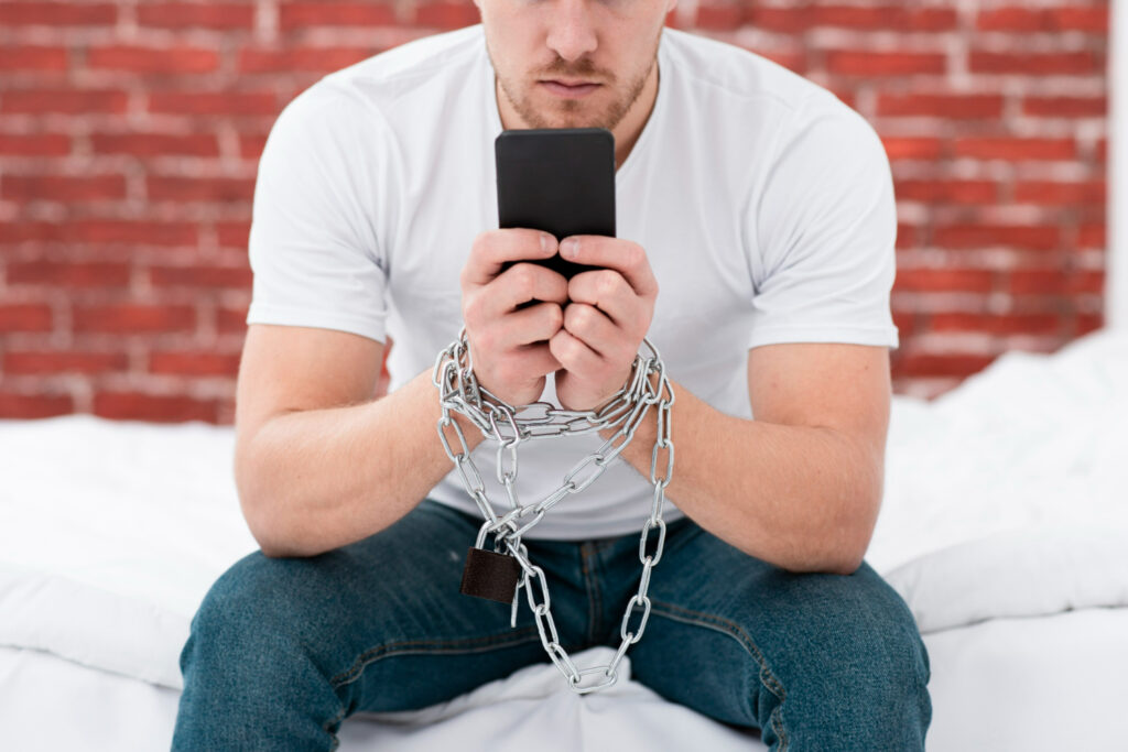 Hombre sentado con cadenas en las manos mirando su smartphone