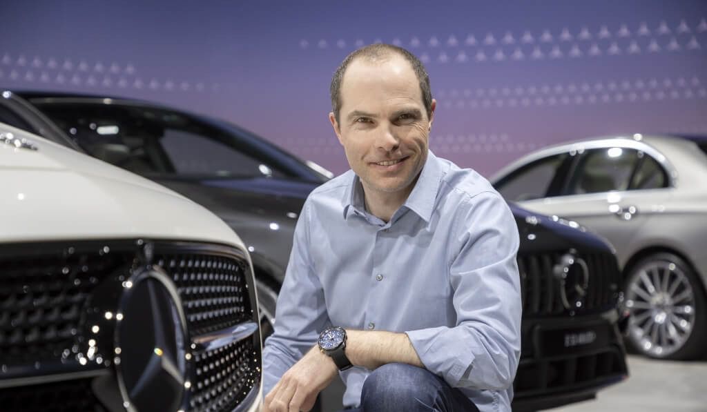 Persona sonriente junto a coches Mercedes en un evento automovilístico