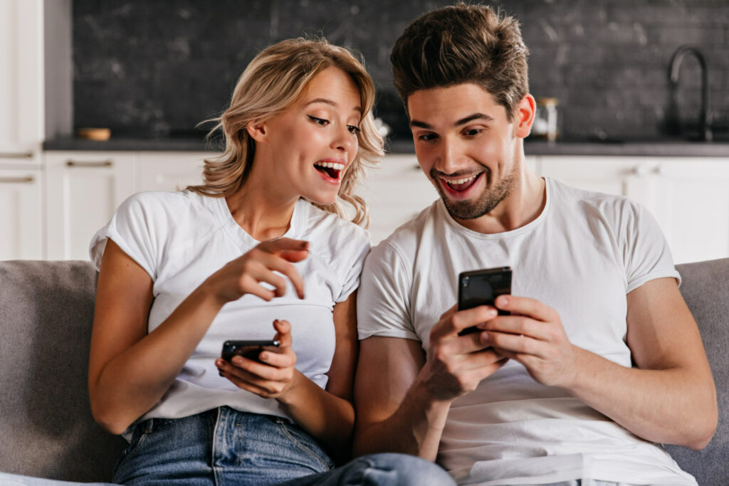 Pareja sonriente usando teléfonos móviles en un sofá