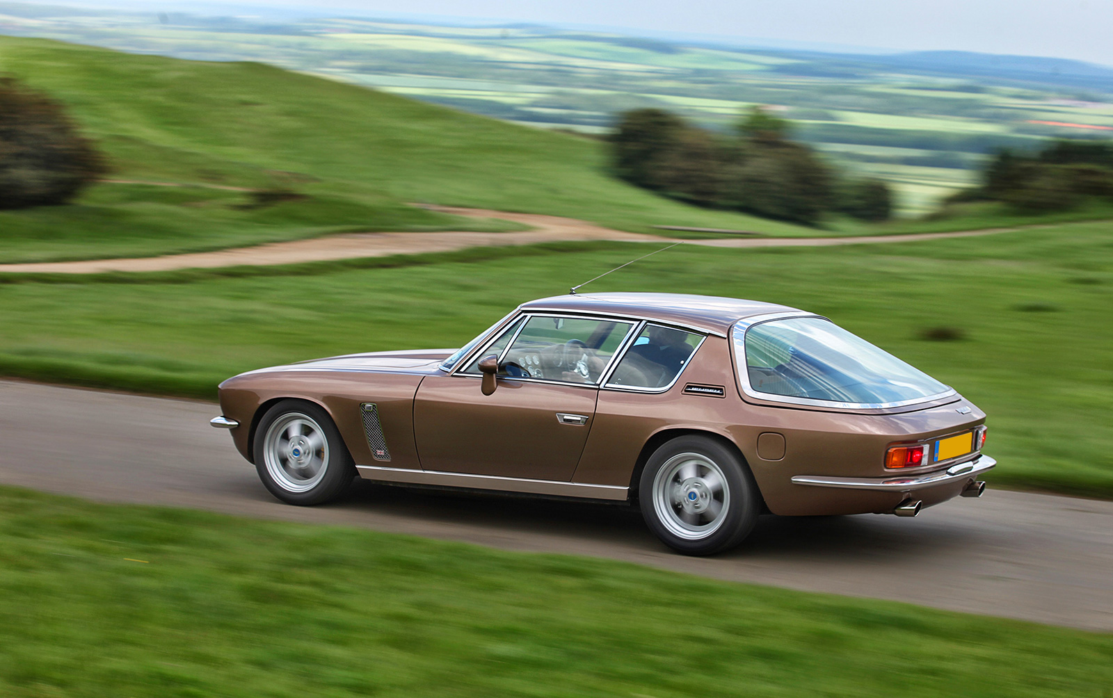 Coche Jensen GT V8 en un paisaje verde, capturando su diseño elegante.