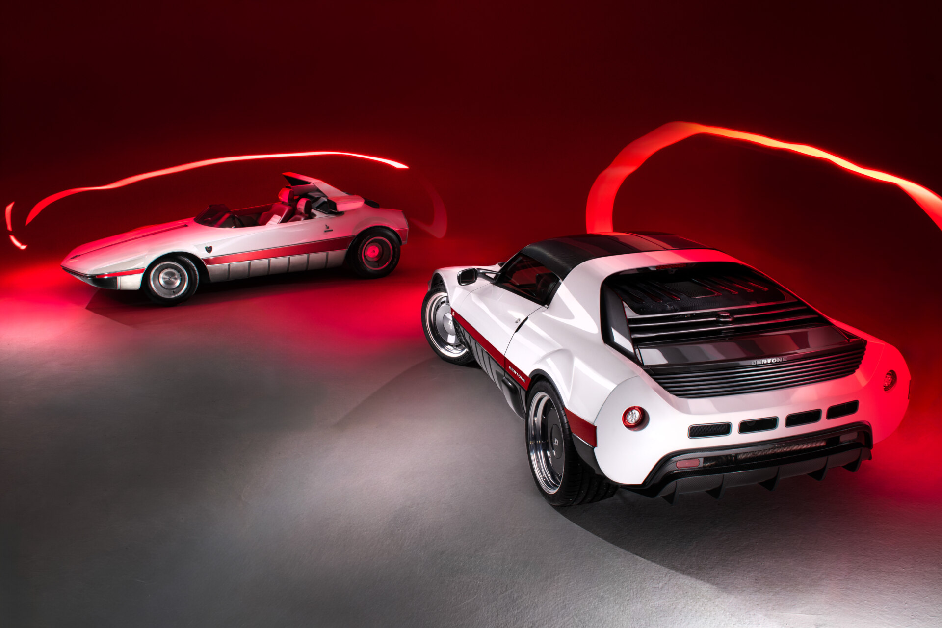Dos coches Bertone Runabout, uno descapotable y otro Targa, en fondo rojo