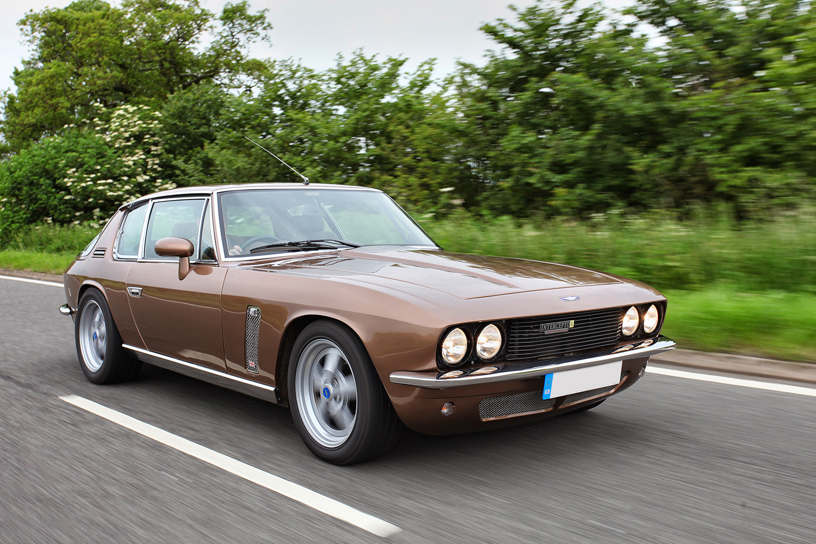 Coche Jensen GT V8 en movimiento por carretera con paisaje verde de fondo