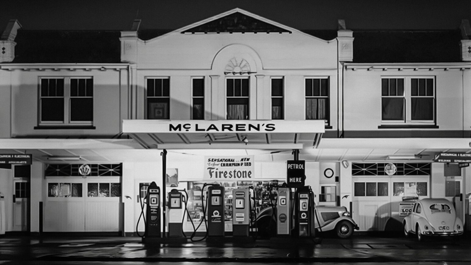 Antigua estación de servicio McLaren con bombas de gasolina y vehículos clásicos.