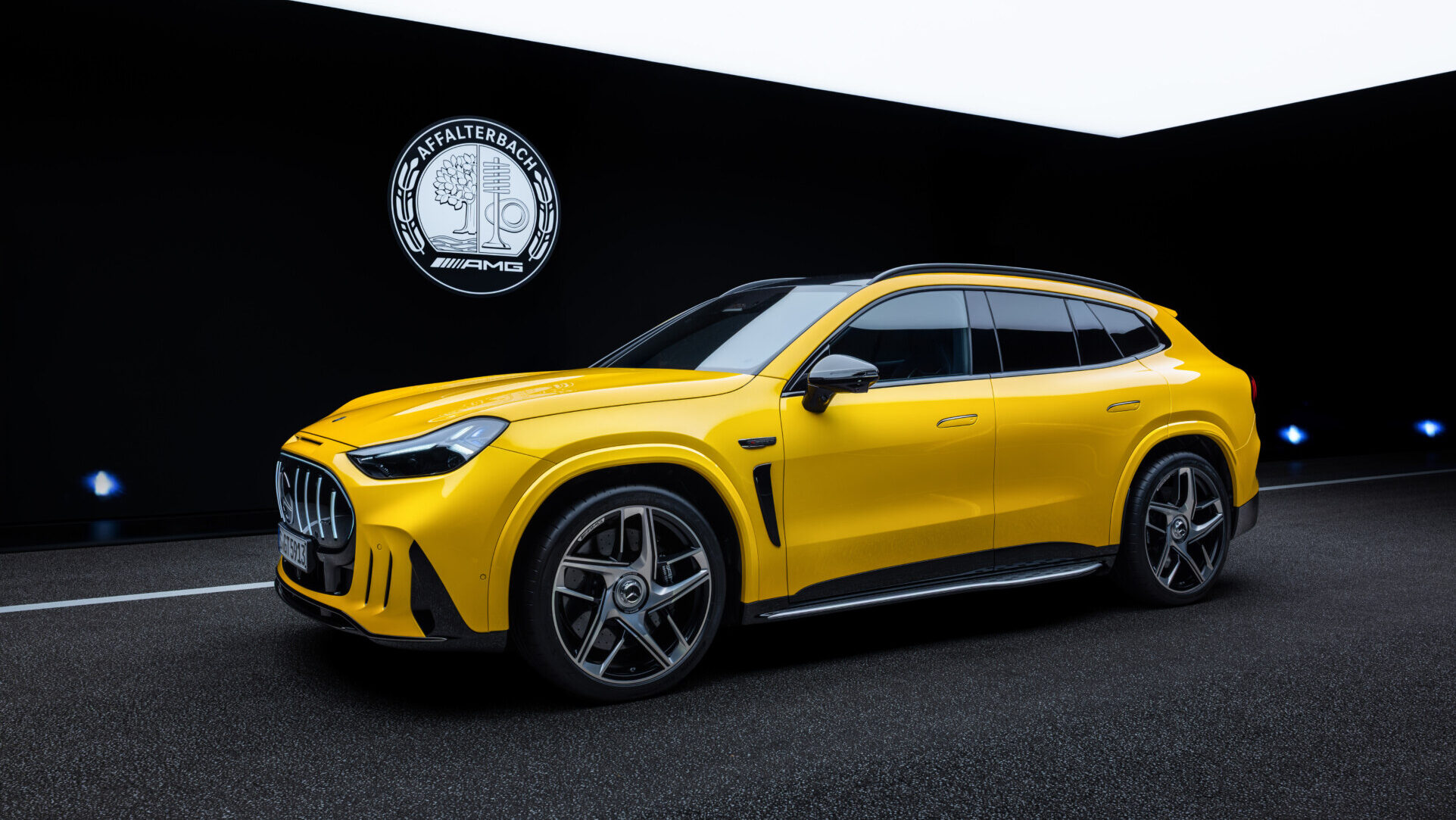 SUV amarillo de Mercedes-AMG visto de perfil en un espacio de exposición oscuro.
