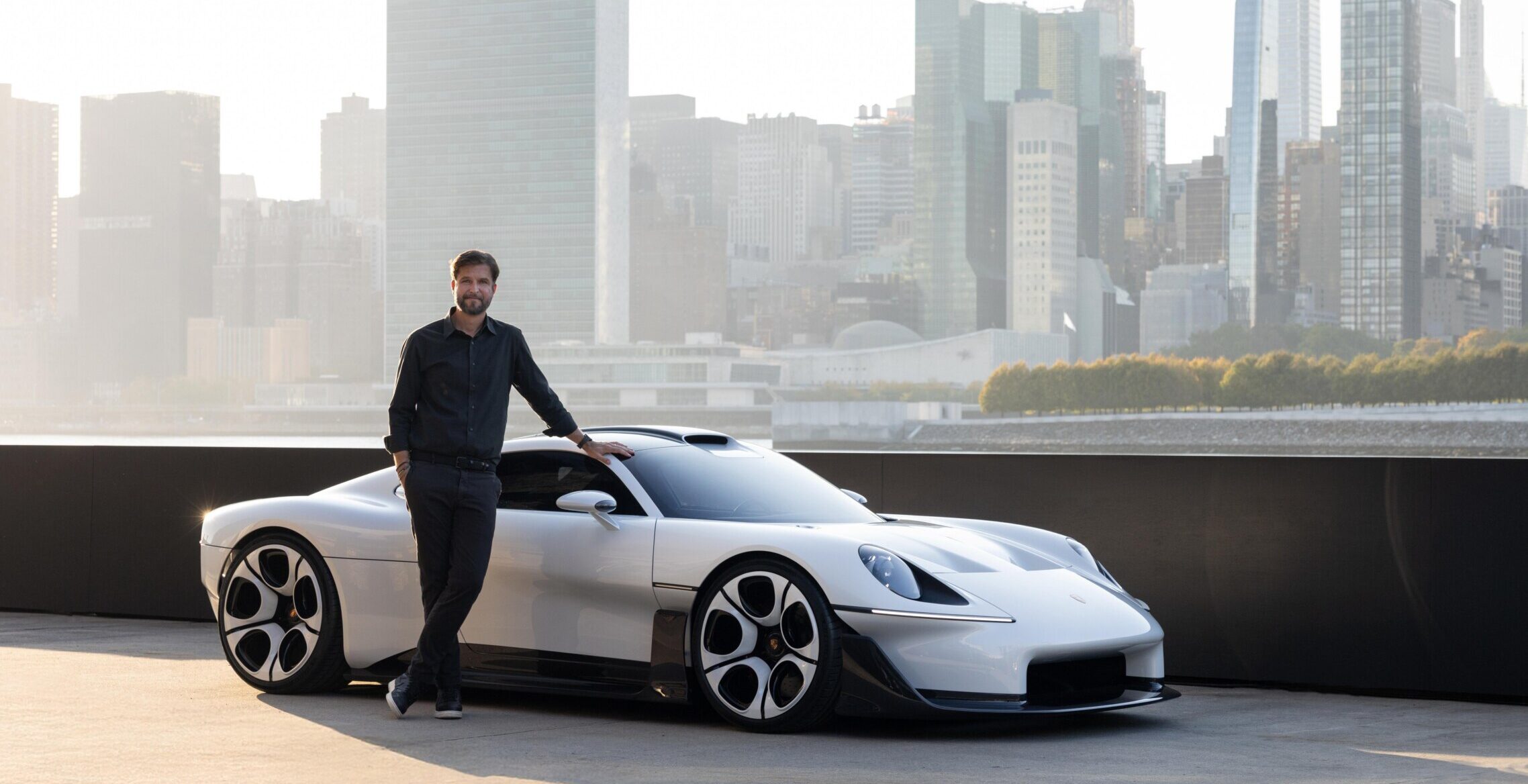 Hombre junto a un deportivo blanco Porsche Mission S, con rascacielos al fondo.